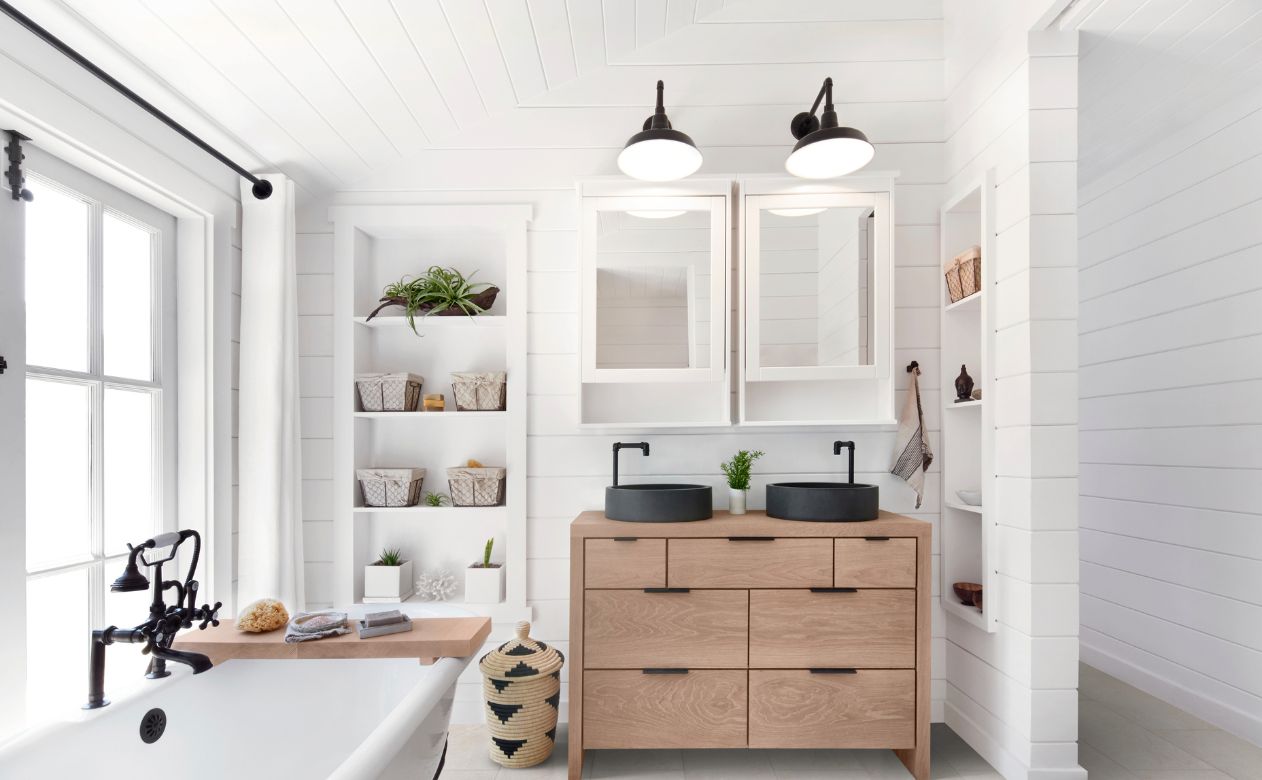 bright bathroom with bathroom fixtures including white freestanding tub, black sinks and faucets