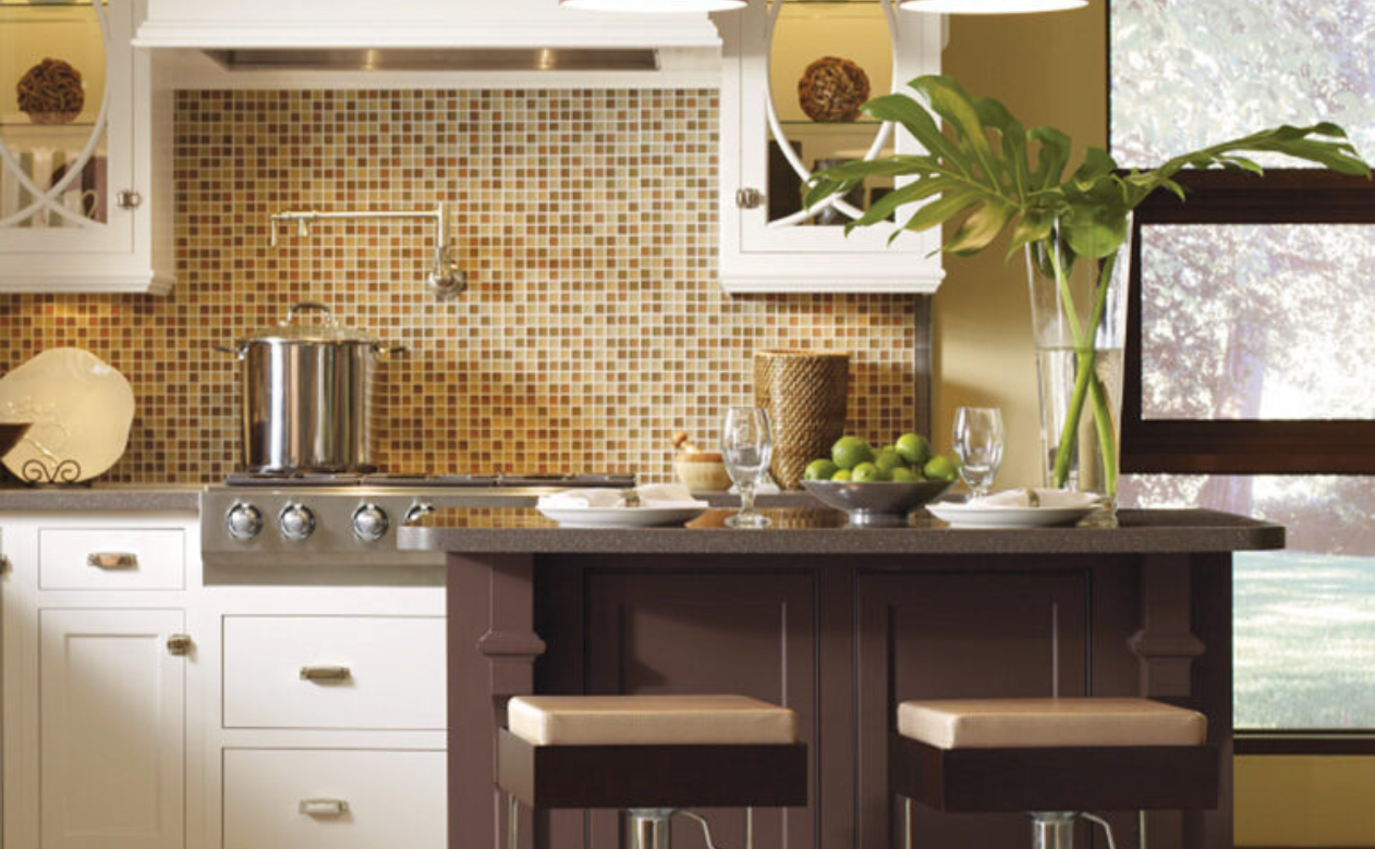 Modern kitchen with a mosaic backsplash, white cabinets, stainless steel appliances, and a dark island set with limes, plates, and a vase of green leaves.